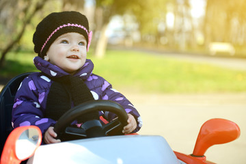 Happy cute little girl in park driving a car