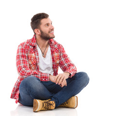 Smiling man in lumberjack shirt sitting with legs crossed