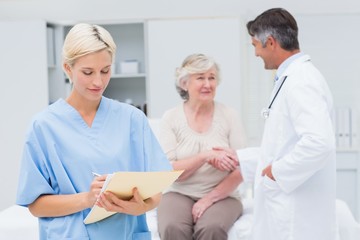 Female nurse making reports while doctor and patient talking