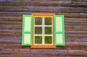 Alpine wooden dark house facade with window and green shutter