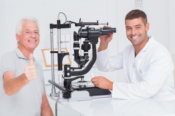 Senior man showing thumbs up while sitting with optician