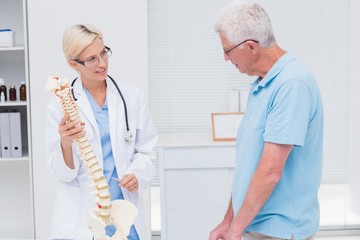 Fototapeta premium Orthopedic doctor explaining anatomical spine to senior man