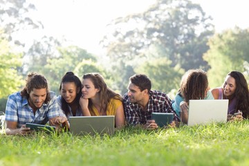 Smiling friends in the park using tablet pc and laptop