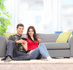 Couple drinking wine seated by a sofa at home