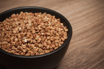 Buckwheat in black bowl on wooden background.