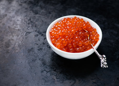 Salmon caviar in white bowl on dark background