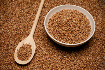 buckwheat groats on wooden spoon next to bowl