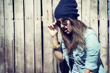 beautiful cool girl in hat and sunglasses against grunge wooden