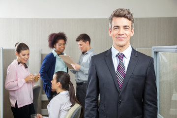 Confident Manager With Employees Discussing In Background