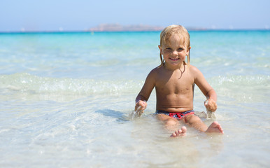 Cute little smiling boy plays at tropical beach