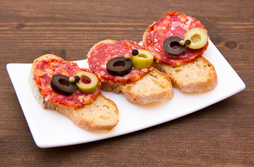 Bruschetta with salami and olives on wooden table