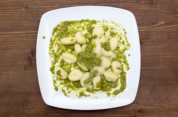 Gnocchi with basil pesto on wooden table seen from above