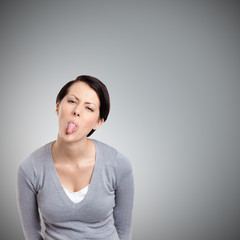 Young pretty woman shoots out tongue, isolated on grey