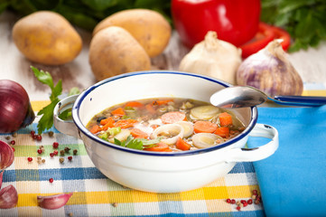 Vegetable soup in a metal bowl on a rural rustic wooden table.