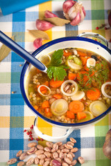 Vegetable soup in a metal bowl on a rural rustic wooden table.