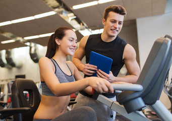 happy woman with trainer on exercise bike in gym