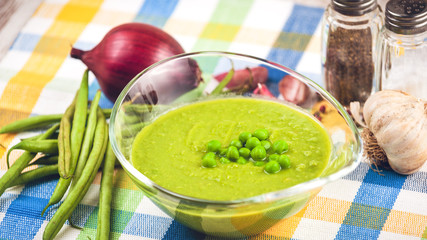 Green pea soup in a transparent bowl on a colorful tablecloth.