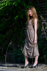 Young woman standing against rocks wall with long leaves