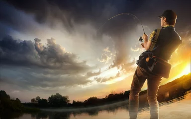 Poster Young man fishing at dramatic sunset © vitaliy_melnik