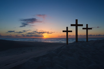 Three crosses on sand dune next to the ocean with a cloudy sunri