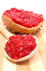 Strawberry jam on wooden spoon and whole wheat bread