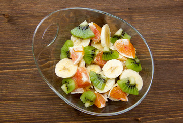 Bowl with cut fruit on wooden table top view