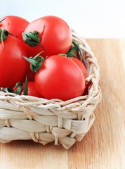 Tomatoes in straw basket wooden background