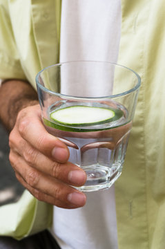 man holding a glass of water with cucumber slice