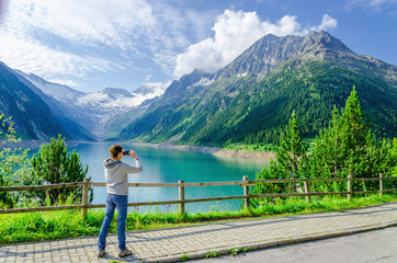 Fototapeta na wymiar Young woman photographing a beautiful alpine lake, Austria