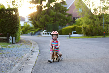Naklejka premium Toddler girl driving wooden tricycle on the street