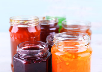 Fototapeta na wymiar Homemade jars of fruits jam on table and color wall background
