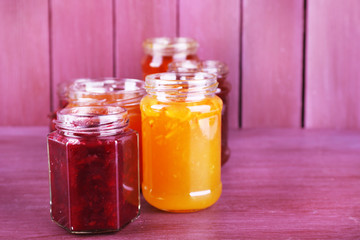 Homemade jars of fruits jam on color wooden background