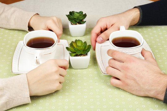Female and male hands with cups of tea, close-up