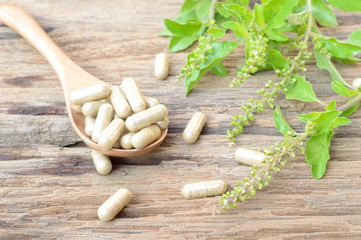 herb capsule with herbal leaf on wooden table