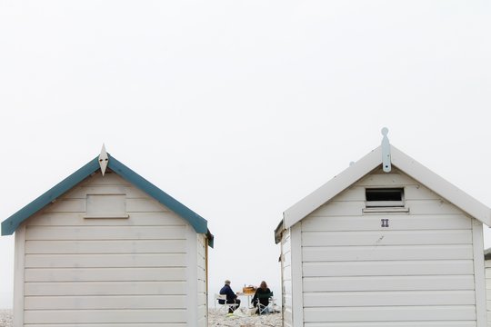 A couple having a picnic next to beach huts on an overcast day