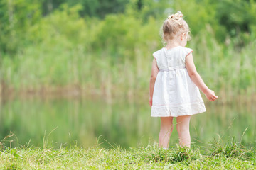 Little girl in light summer dress near forest pond