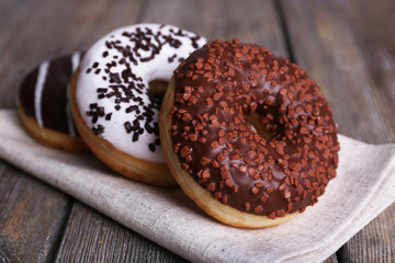 Delicious donuts with icing on napkin on wooden background