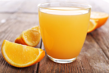 Glass of orange juice with oranges on wooden table close up