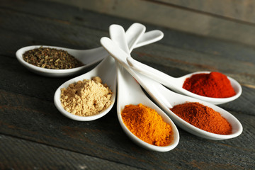 Different kinds of spices in spoons on wooden background