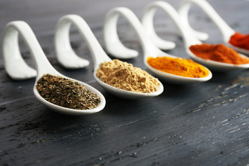 Different kinds of spices in spoons on wooden background