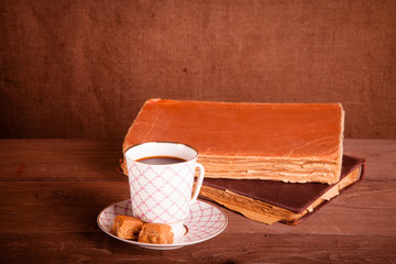 Old books and a cup of coffee with two candies on an old wooden