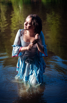 Young beautiful girl in long blue dress standing in the river