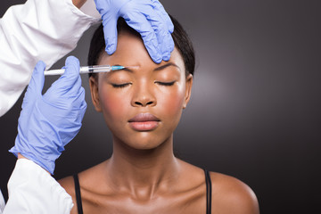 cosmetic doctor injecting african woman forehead