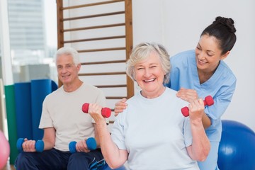 Senior woman lifting dumbbells while sitting with man