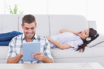 Man using tablet PC while woman listening music on headphones