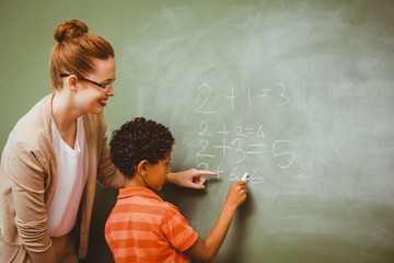Teacher assisting boy to write on blackboard in classroom