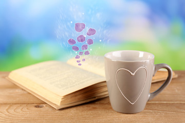 Open book with flying petals on table on bright background
