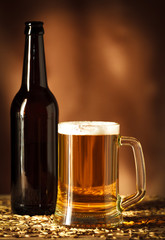Bottle and glass of beer on old wooden table with grain