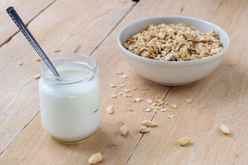 Natural yogurt in little jar with bowl of oat granola on wooden