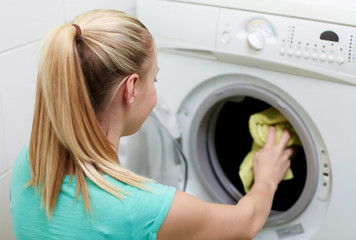 happy woman putting laundry into washer at home